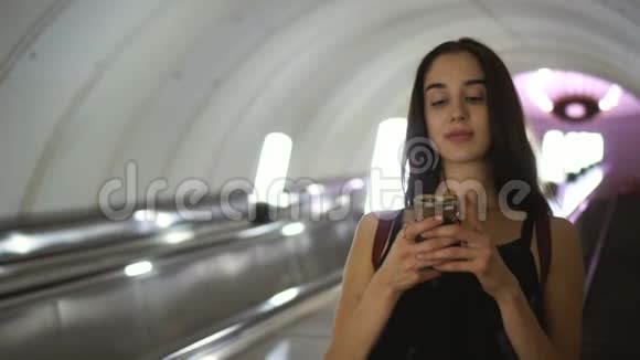美女在地铁自动扶梯下在手机微笑中阅读信息视频的预览图