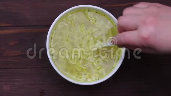 特写镜头一只手用白色塑料叉子搅动面条纸张的容量汤在煮视频的预览图