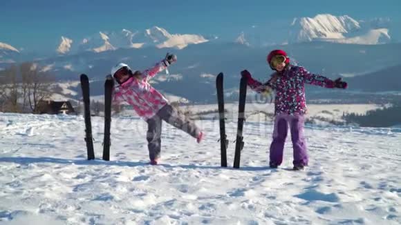 穿着外套戴着头盔的小女孩在雪地上摆着滑雪板背景是山脉视频的预览图