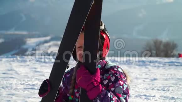 小女孩戴着红色的头盔穿着户外服装在阳光下手持山地滑雪板视频的预览图