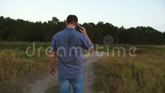 穿着衬衫的男人在智能手机上说话沿着森林的道路行走视频的预览图