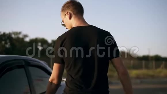 年轻漂亮的男子穿着黑色T恤和太阳镜上车黑色银色轿车准备和女朋友一起去视频的预览图