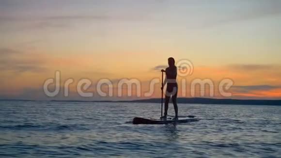 夕阳与女性剪影航行的桨板积极的生活方式观念视频的预览图