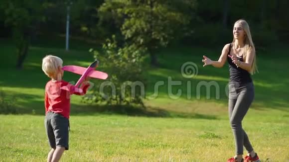 一个年轻女子和她的小儿子在草坪上玩飞机的慢镜头视频的预览图