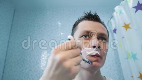 一个人用剃刀在泡沫中剃了他的脸他在镜子前刮胡子视频的预览图