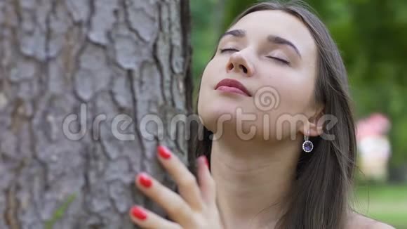 闭着眼睛的女人感觉到树和与自然的合一对生命的热爱快乐视频的预览图