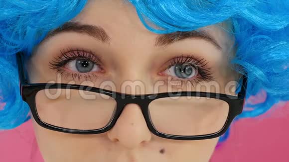 戴着蓝色假发和戴着深红色背景眼镜的女孩的肖像视频的预览图