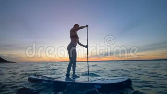 斯利姆女士在她的桨板上航行过开阔的水域夏季趣味动作运动视频的预览图