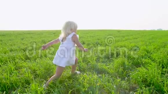 金发可爱的小女孩穿着白色的裙子在绿色的田野上向姐姐跑来微笑着姐妹孩子孩子们视频的预览图