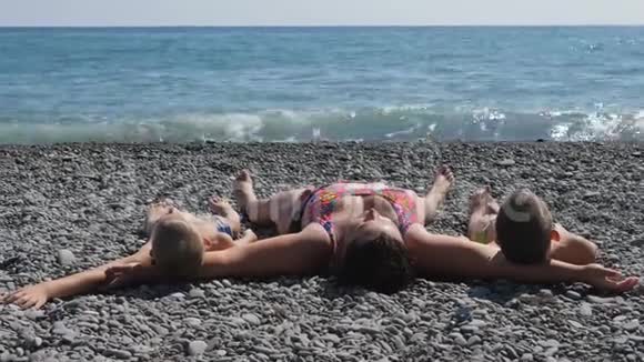 人们躺在海滩上一个有两个孩子的女人躺在石头上海浪在卵石海滩上破碎视频的预览图