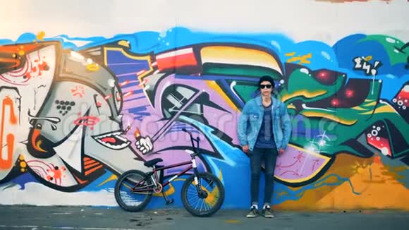 时尚的青少年自行车站在涂鸦墙附近他的自行车在一个现代滑板公园视频的预览图