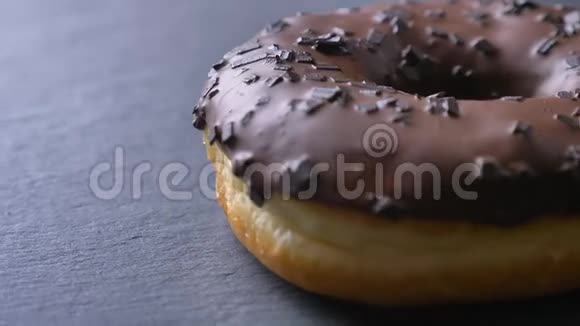 在灰色的桌子背景上用巧克力片慢慢旋转的釉色棕色甜甜圈的特写镜头视频的预览图