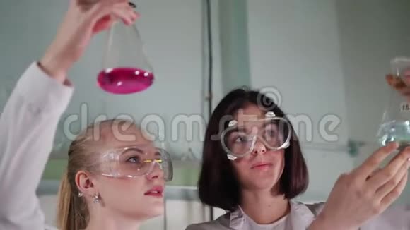 化学实验室两个年轻的实验室技术人员把桌上的烧瓶拿在手里看着它视频的预览图