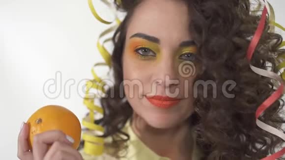 特写年轻俏皮的微笑女孩与明亮的化妆抱着橙色的肖像慢动作视频的预览图