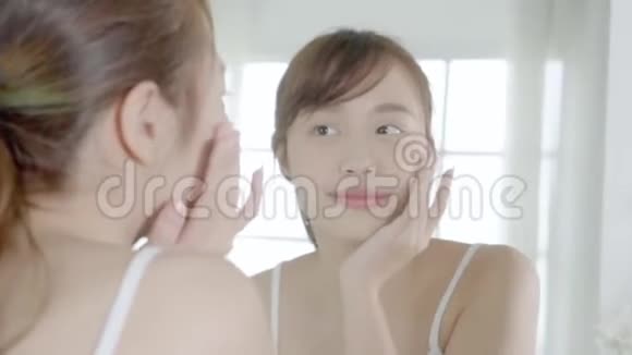 美丽的年轻亚洲女性快乐地将面霜或乳液与保湿剂一起涂抹在皮肤上视频的预览图