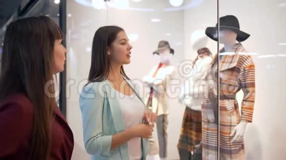 购物周末时尚女孩在打折和打折的季节与模特们讨论橱窗附近的时尚服装视频的预览图