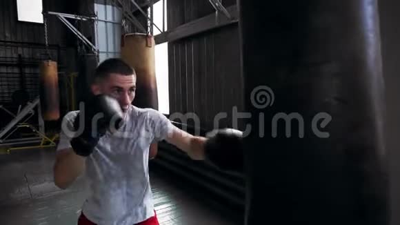 穿T恤和红衬衫的白人男拳击手在健身房锻炼用拳击袋练习踢腿和踢腿视频的预览图