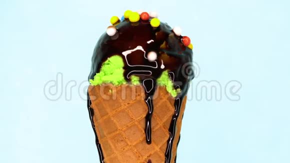 绿色开心果洒在华夫饼锥上旋转在蓝色背景上液体巧克力酱浇在上面视频的预览图
