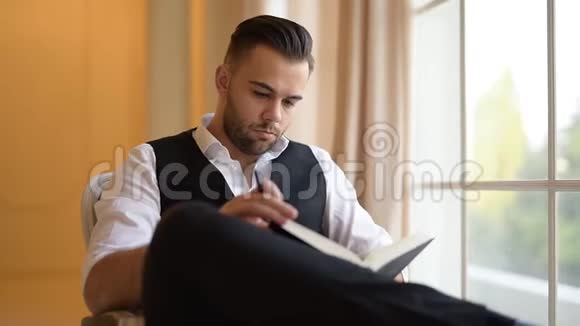 一个年轻人坐在扶手椅上翻过一本关于窗户背景的书视频的预览图