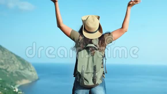 活动背包女旅行者戴着帽子和太阳镜享受着惊人的海景举手视频的预览图