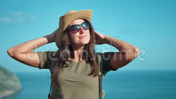 戴着帽子戴着太阳镜的女徒步旅行者欣赏太阳举起双手竖起大拇指的肖像视频的预览图