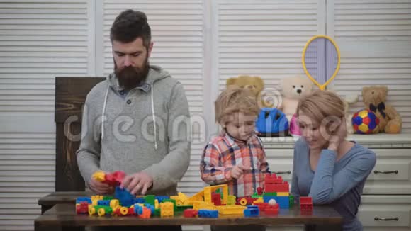 在游戏室的年轻家庭热爱家庭观念妈妈爸爸和男孩用塑料积木搭建玩具父母和儿子视频的预览图
