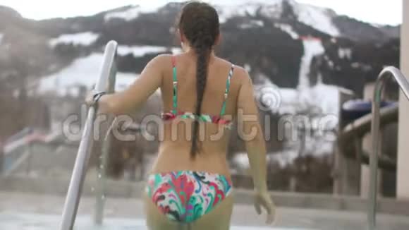 冬天穿着泳衣带着长长的辫子的漂亮黑发女人从炎热的游泳池里出来她身上有蒸汽视频的预览图