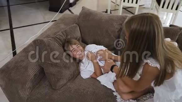 漂亮的女孩和她的妹妹在家玩得很开心可爱的少女留着长发在妹妹身上挠痒痒视频的预览图