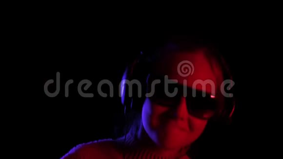 快乐的少年女孩戴着黑色太阳镜和耳机在黑色工作室听音乐快乐女孩享受音乐视频的预览图