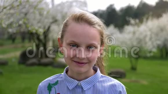 可爱的白种人小女孩蓝眼睛穿着一件漂亮的衬衫春天站在公园里视频的预览图