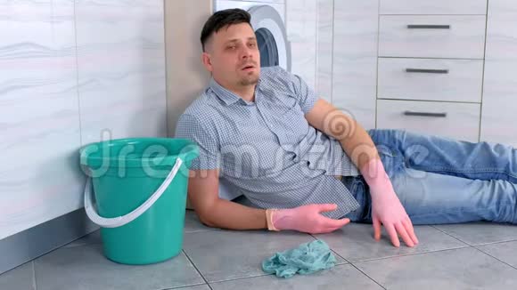 穿着橡胶手套的疲惫的人从厨房地板上的清洁中休息视频的预览图