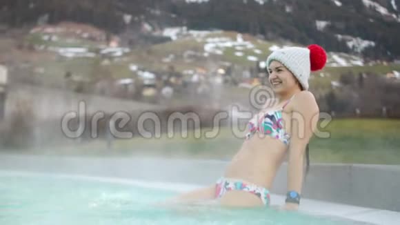 在冬天穿着针织帽子和泳衣的布鲁内特在雪地的背景下潜入了一个炎热的游泳池视频的预览图