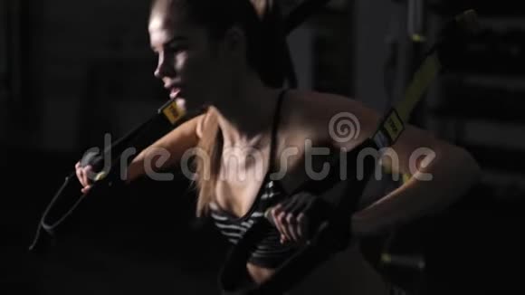 漂亮的女人在黑暗的健身房里用三角带做运动视频的预览图