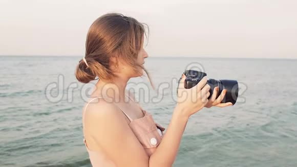 年轻的女摄影师沿着海滨散步拍照片女孩在日落时度假爱好自负视频的预览图