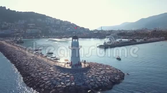站在石墩尽头海水环绕的小灯塔附近行走的人的鸟瞰图视频的预览图