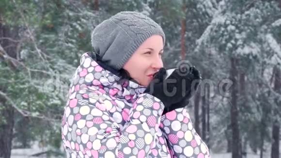 一个女游客站在冬天的森林或公园的雪天喝热茶从一个杯子特写镜头视频的预览图