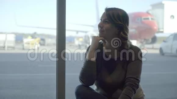 年轻的女游客在机场透过窗户看飞机视频的预览图
