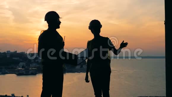 一男一女的建筑师建筑工人建筑工人在日落时正在交谈视频的预览图