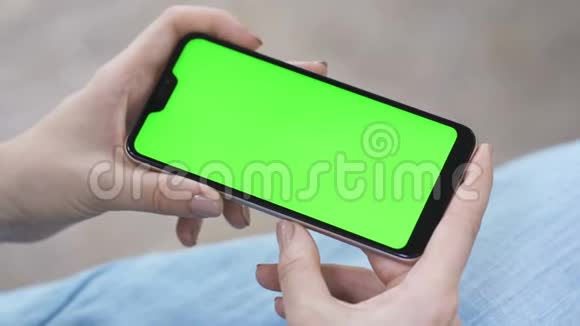 女孩水平地拿着一部智能手机在屏幕上观看视频追踪绿色屏幕智能手机视频的预览图