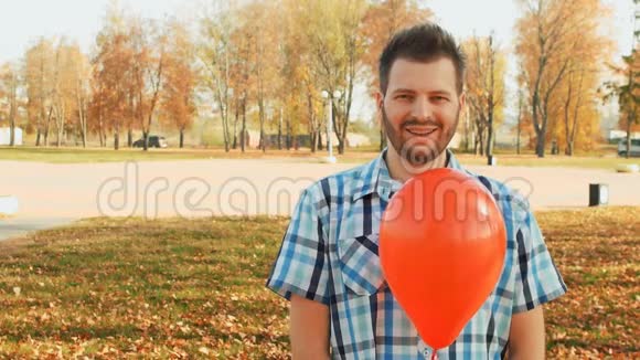 一个满脸胡须的男人手里拿着一个红色的气球站着视频的预览图