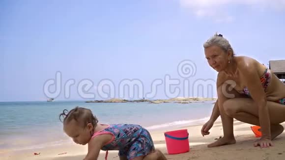祖母和孙女在沙滩上玩海滩玩具一个小女孩沿着海滩爬行视频的预览图