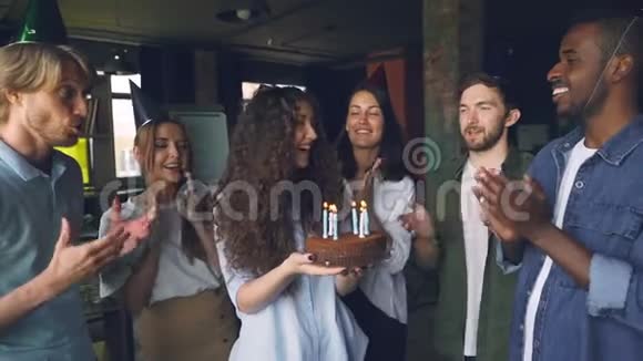当同事站着的时候戴着派对帽拿着蛋糕吹着蜡烛的漂亮女孩动作缓慢视频的预览图