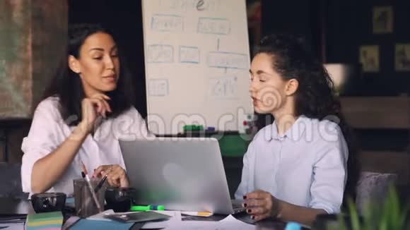 有魅力的女性同事正在谈论和使用笔记本电脑坐在共享办公室的办公桌上现代技术视频的预览图