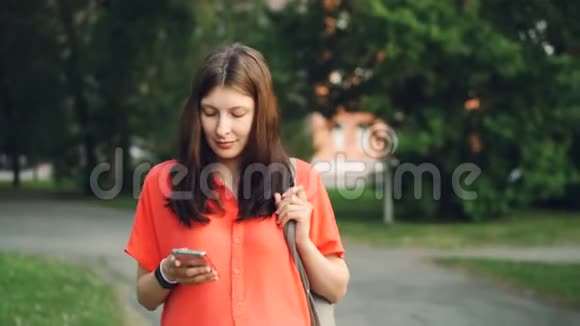 漂亮的孕妇在夏天用智能手机看公园里的屏幕行走现代科技健康视频的预览图