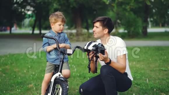 照看孩子的父亲手里拿着自行车头盔一边和他可爱的儿子交谈一边解释安全规定视频的预览图