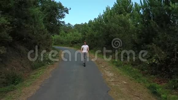 在森林里的路上骑着电动滑板车的年轻人视频的预览图
