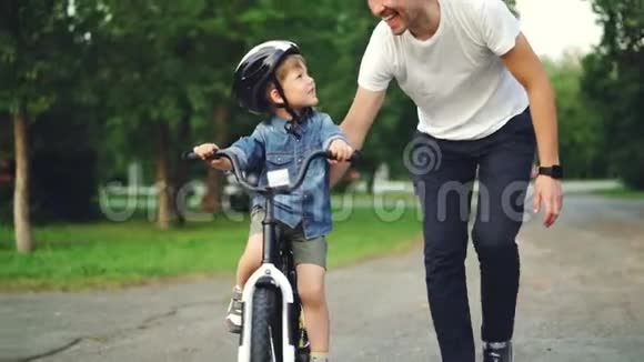 爱动作爱爸爸教他可爱的儿子在公园里骑自行车拿着自行车和孩子说话视频的预览图