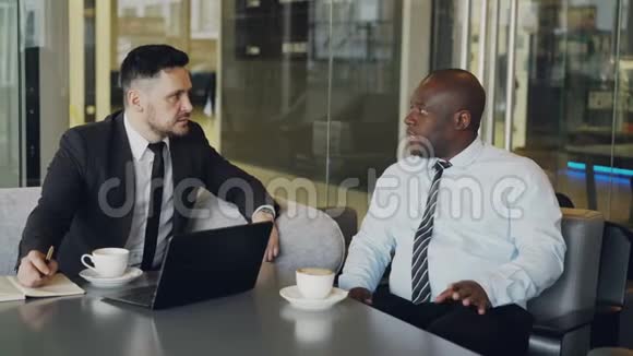 两位自信的商人在现代玻璃咖啡馆的会议上讨论伙伴关系视频的预览图