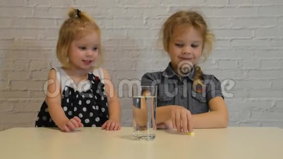 一个两个孩子慢慢的女孩看起来可溶性泡腾维生素C在一杯水中视频的预览图