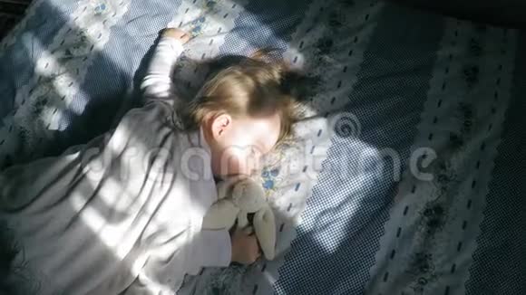 可爱的金发小女孩睡在床上她的肚子被阳光照亮带着一只泰迪兔子视频的预览图